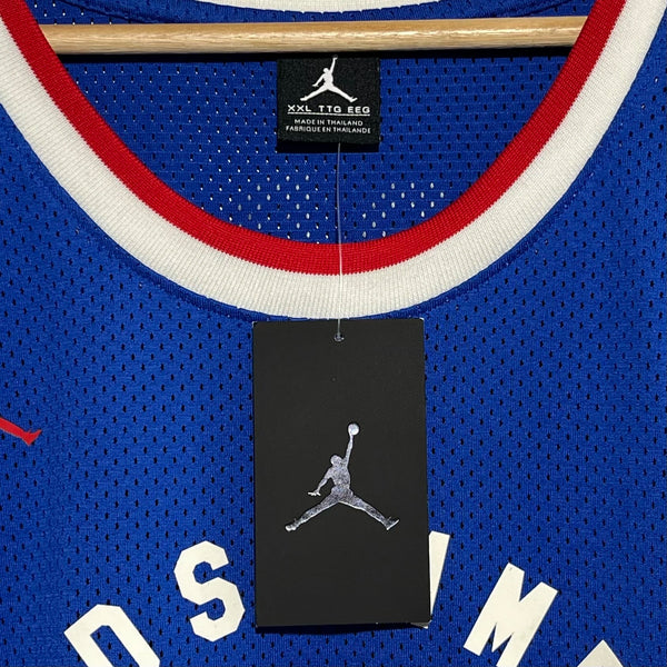 Blue basketball jersey with red and white trim, featuring a Jordan Brand logo on a hanger.