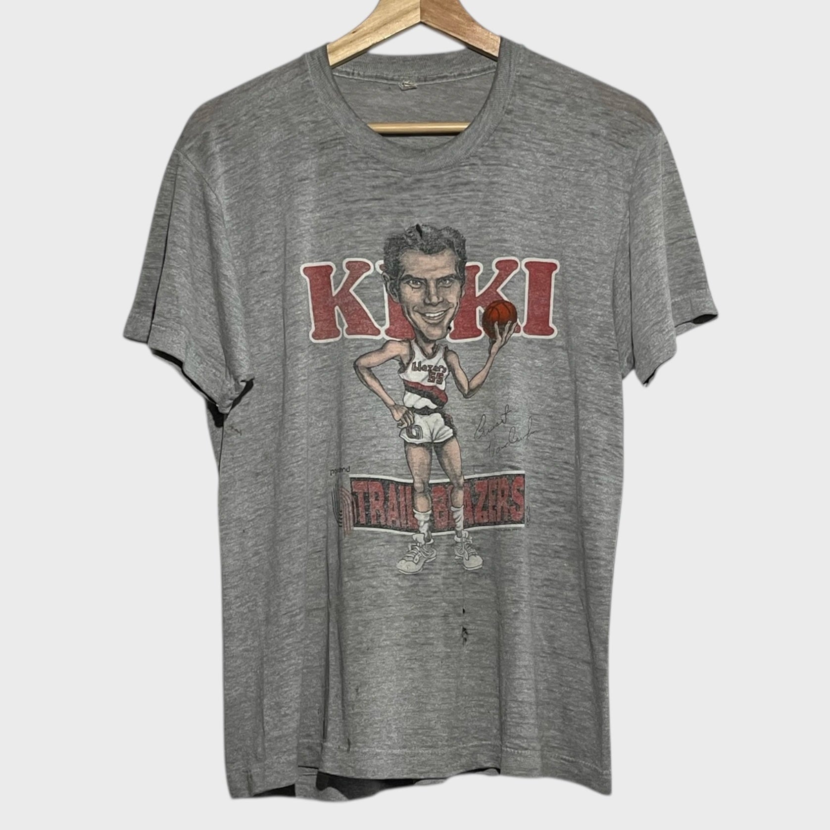 Gray t-shirt with a graphic of a basketball player and 'Kiki' text on a hanger.