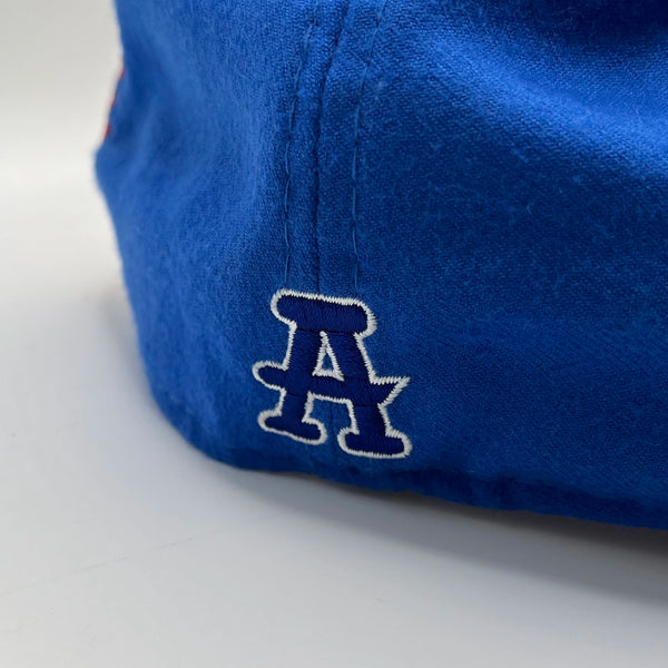 Back of a blue fitted baseball cap with a white embroidered letter 'A' on a light gray background