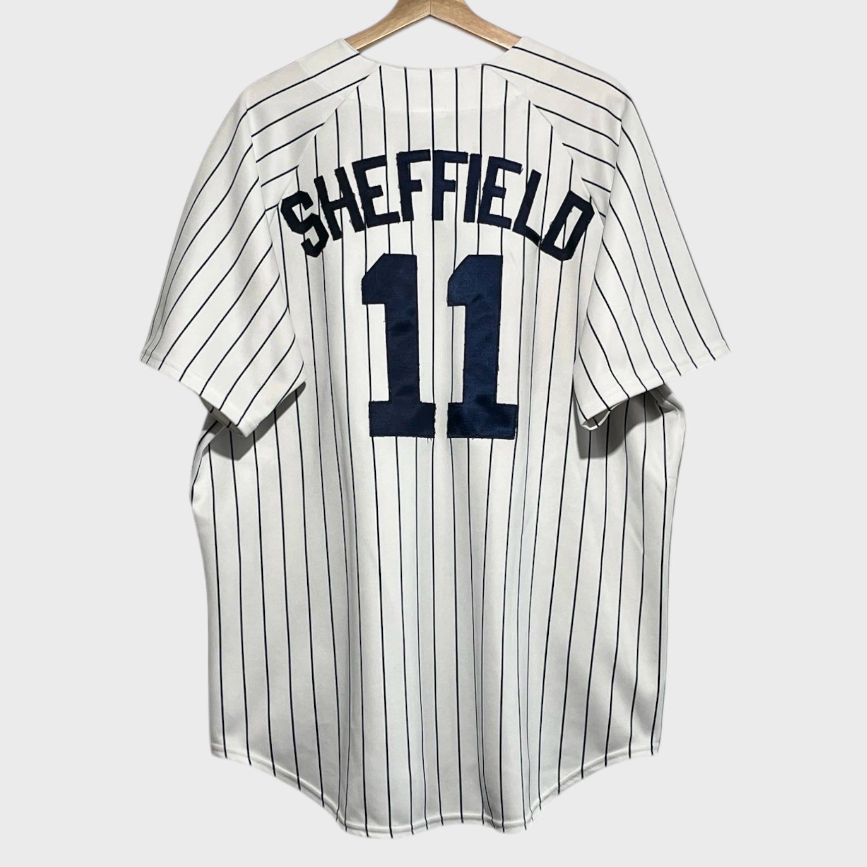 Back of a white baseball jersey with the name “Sheffield” and number “11” in navy blue appliqué.