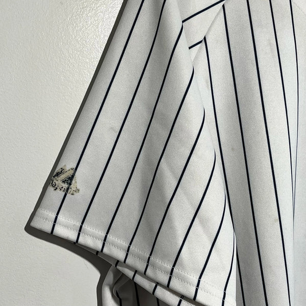 White baseball jersey sleeve with black pinstripes and a small emblem on a light gray background