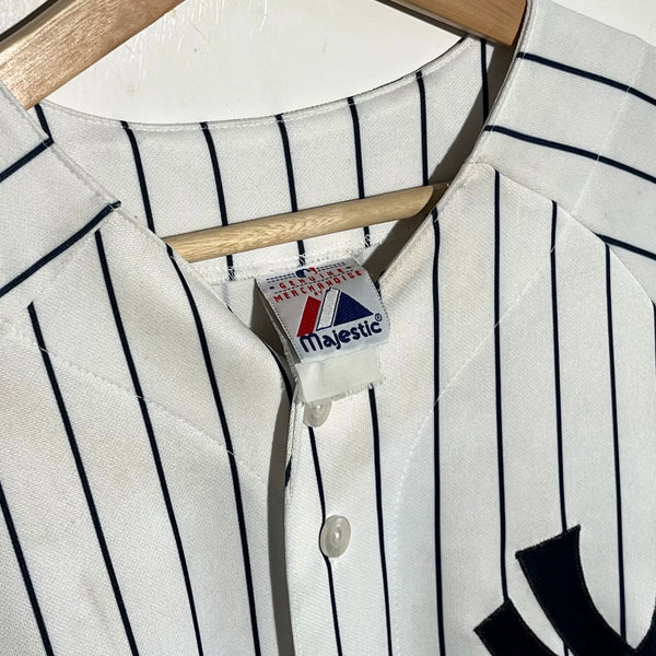 Close-up of a white baseball jersey with black pinstripes and a Majestic label on a hanger.